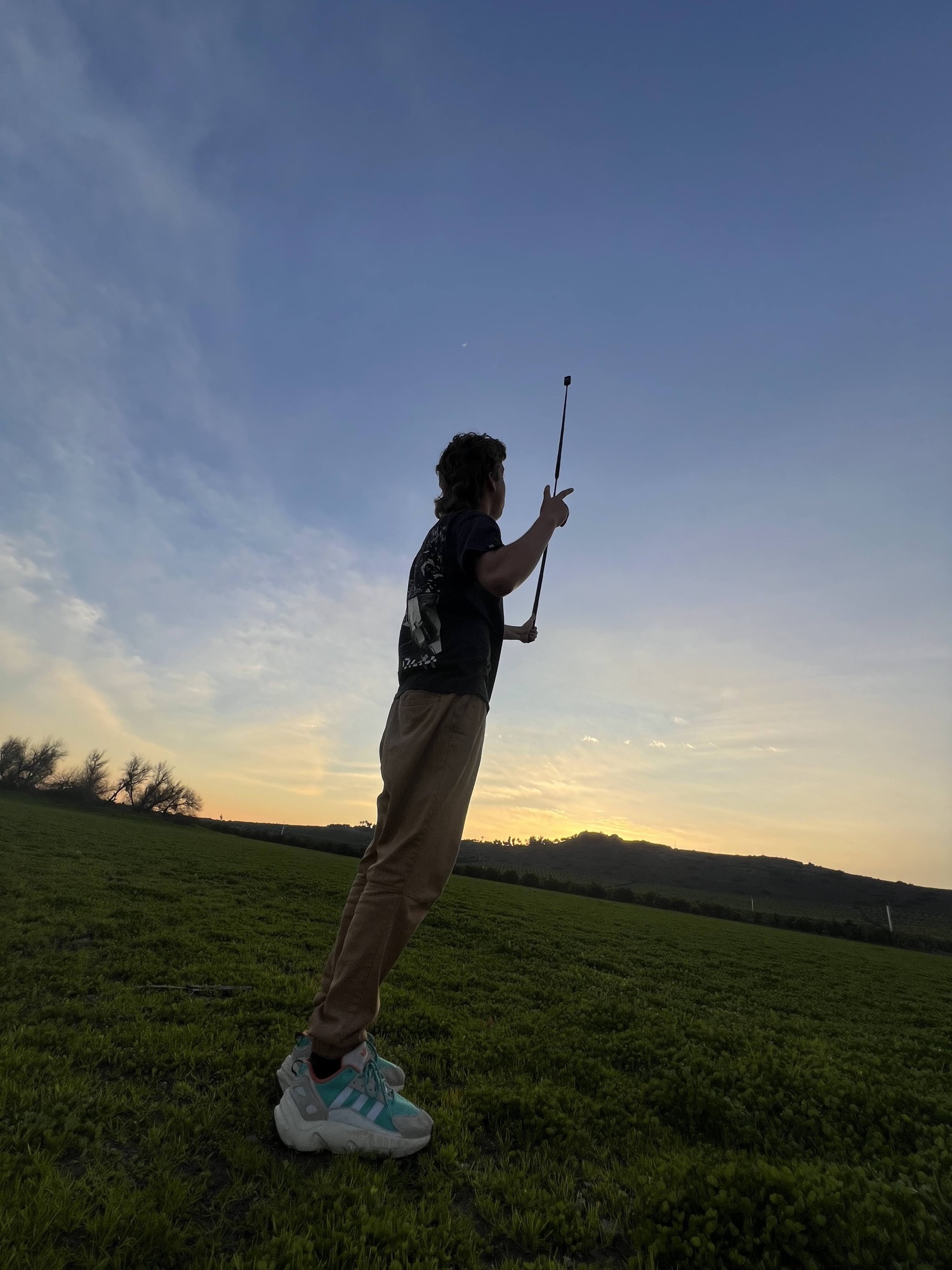 Silhouette of Finn extending a camera pole toward the last of the sunset over a field