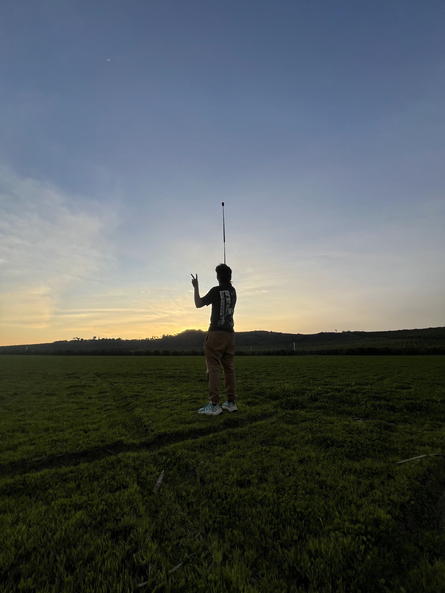 Wide view of a green California field at dusk with the operator small in frame under an open sky
