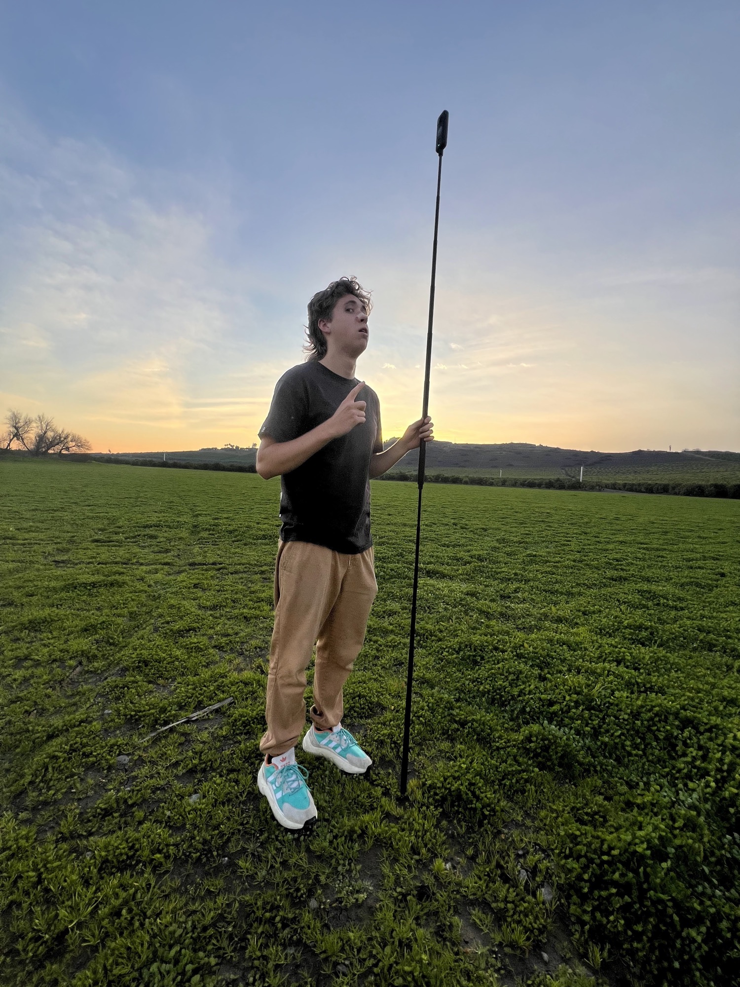 Finn looking up past a 360 camera pole while setting a shot in a green field